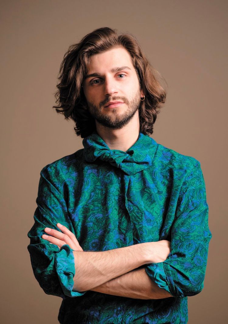 Xavier Gould in a blue and green patterned top, arms crossed, looking into the camera.